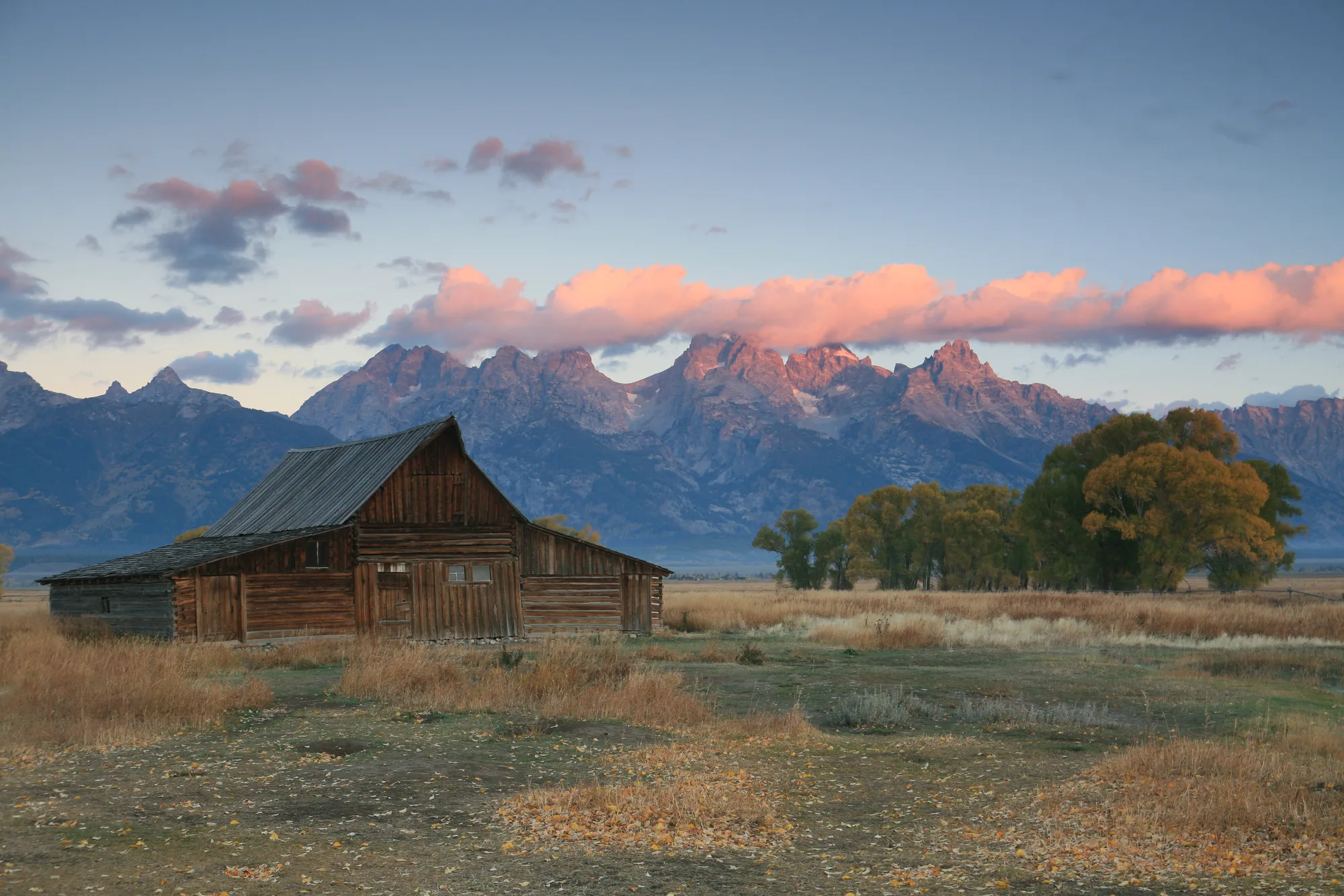 Weathered log barn with the Teton Range rising behind it, similar to the T.A. Moulton Barn